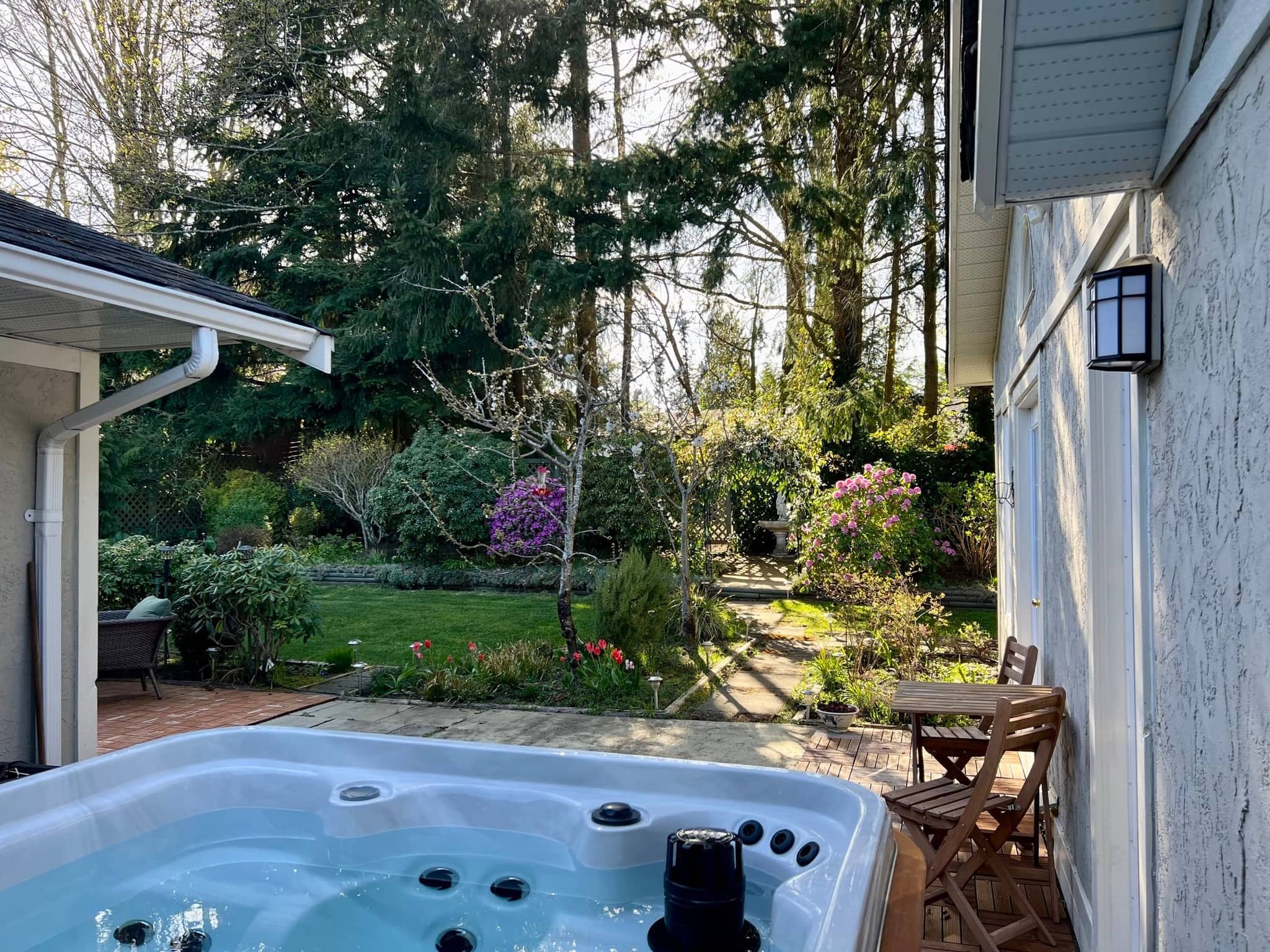 View from the private hot tub across a spring garden with rhododendrons and tall evergreens