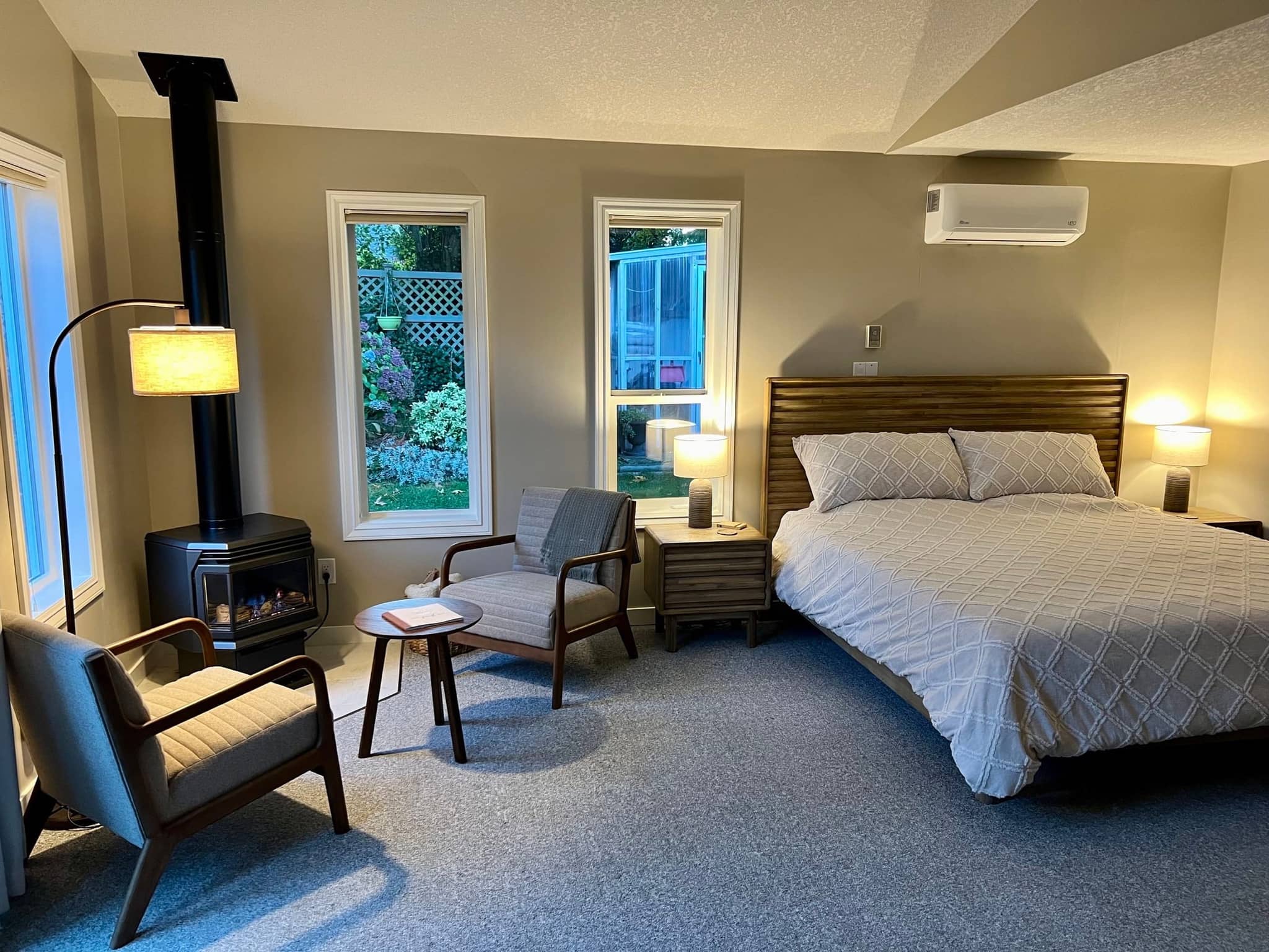 King bedroom with nightstands, reading chair and large windows onto the garden
